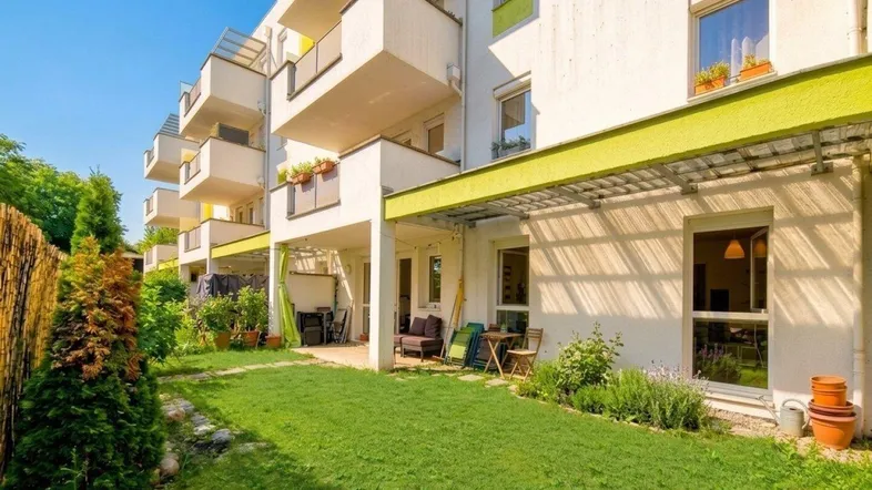 Gepflegter Gartenbereich mit Rasenfläche und überdachter Terrasse vor einem modernen Wohngebäude.