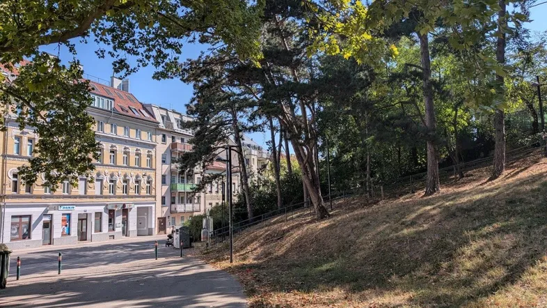 Grüne Umgebung mit Bäumen und einem Bürgersteig neben einem Wohngebäude.