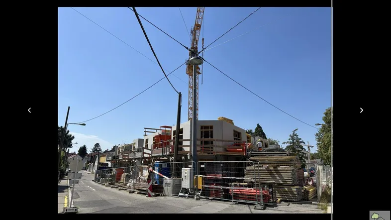 Baustelle eines Neubaus mit Kran und Baumaterialien unter blauem Himmel.