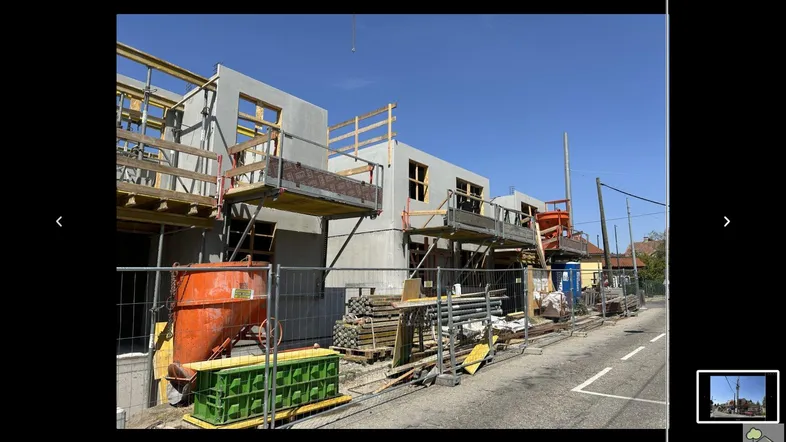 Baustelle eines im Bau befindlichen Gebäudes mit Gerüst und Baumaterialien unter blauem Himmel.