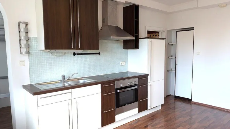 Moderne Küche mit dunklen Holzschränken, weißer Arbeitsplatte und integrierten Geräten, auf einem Holzboden.