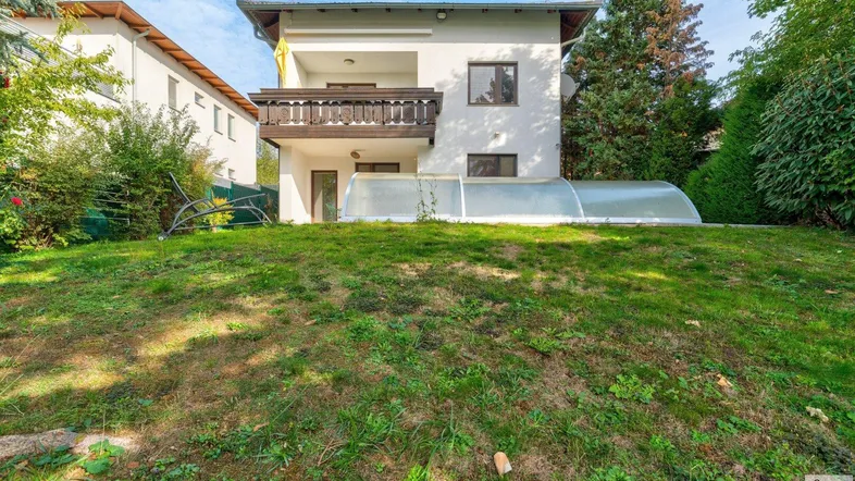 Hinteransicht des Hauses mit großem Garten, überdachtem Pool und Balkon im Obergeschoss.