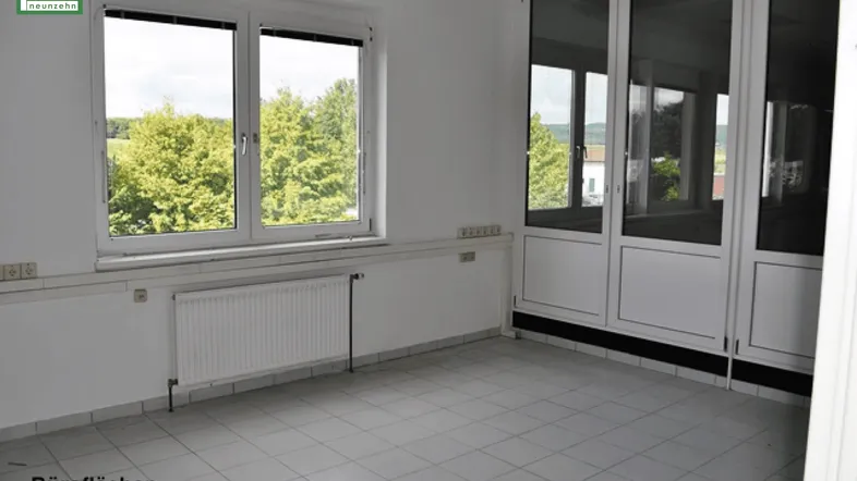 Helles Büro mit großen Fenstern, die einen Blick ins Grüne bieten, und einem Fliesenboden.