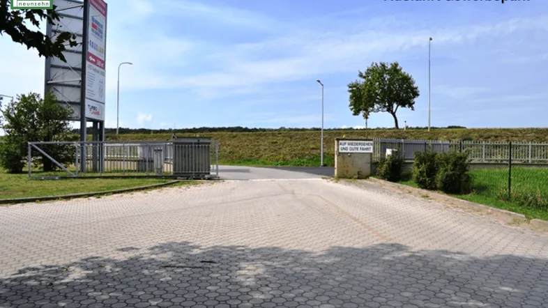 Ausfahrt eines Gewerbeparks mit gepflastertem Weg, Zaun und einem Schild mit Abschiedsgruß.