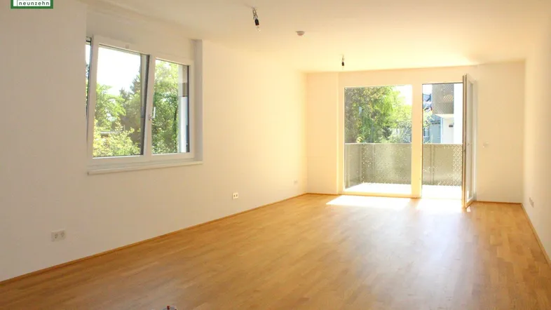 Helles Wohnzimmer mit Parkettboden, großen Fenstern und Zugang zum Balkon.