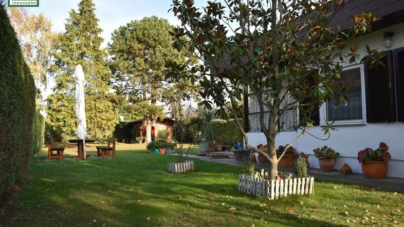 Gepflegter Gartenbereich mit Rasenfläche, Bäumen und Sitzgelegenheiten neben dem Haus.