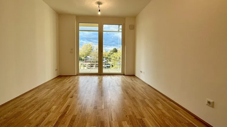 Helles, leeres Zimmer mit Parkettboden und Zugang zu einem Balkon, ideal als Wohn- oder Schlafzimmer.