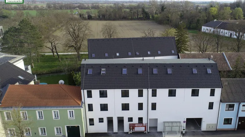 Luftaufnahme eines modernen Wohngebäudes mit umliegender Landschaft und weiteren Häusern.