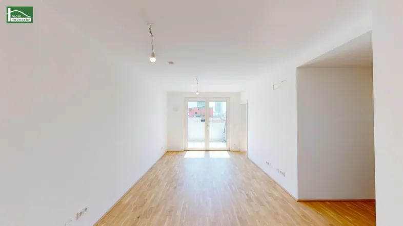 Helles, leeres Wohnzimmer mit Parkettboden und Zugang zu einem Balkon oder einer Terrasse.