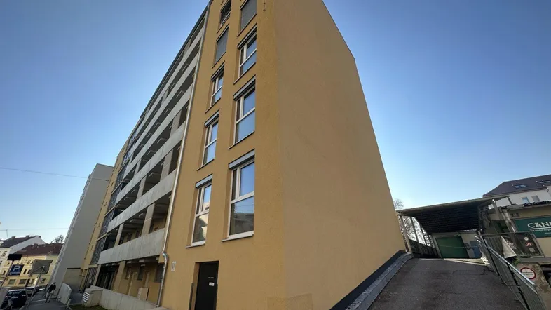 Seitenansicht eines modernen Wohngebäudes mit gelber Fassade und Tiefgaragenzufahrt.