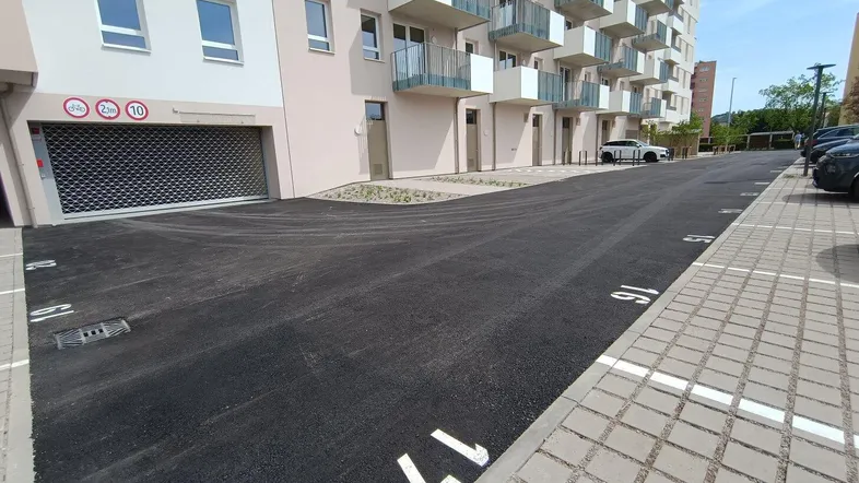 Moderne Wohnanlage mit Balkonen, Zufahrt zur Tiefgarage und Außenstellplätzen auf dem Gelände.