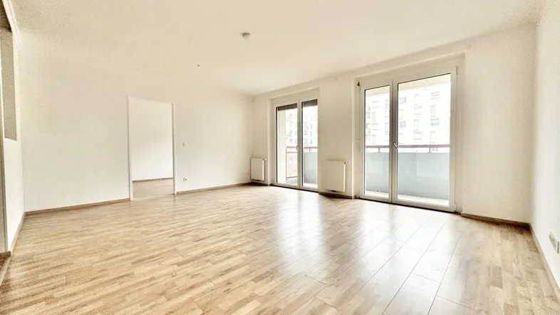 Helles, leeres Wohnzimmer mit Parkettboden und Zugang zu einem Balkon, bereit zum Einzug.