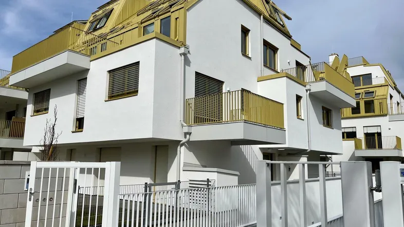 Moderne Wohnanlage mit weißer Fassade, goldenen Dächern und Balkonen, umgeben von einem weißen Zaun.
