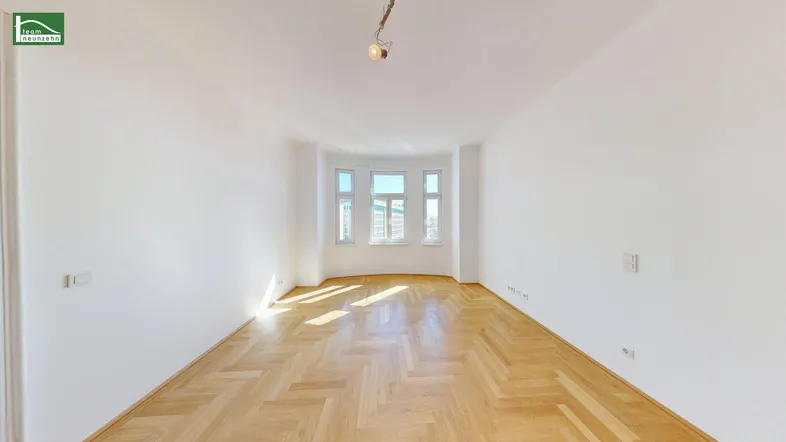 Helles Zimmer mit Fischgrätparkett und Erkerfenstern, durchflutet von natürlichem Sonnenlicht.