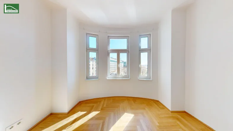 Leerer Raum mit Fischgrätparkett und einem markanten Erkerfenster, das den Raum mit Licht füllt.