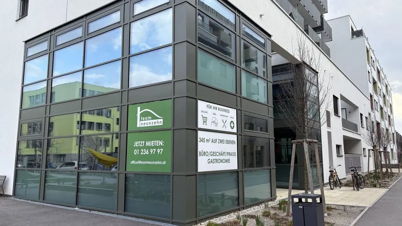 Modernes Geschäftsgebäude mit großen Glasflächen und Werbeschildern an der Fassade in urbaner Umgebung.