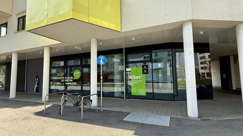 Moderne Außenansicht eines Geschäftsgebäudes mit großen Glasfronten und einem gelben Balkon.