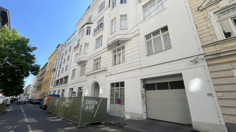 Weißes Mehrfamilienhaus mit klassischer Fassade und Garageneinfahrt an einer Stadtstraße.
