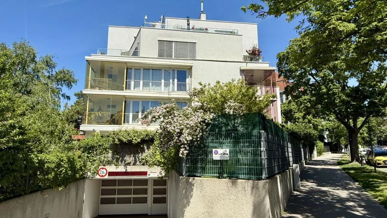 Modernes Mehrfamilienhaus mit Tiefgaragenzufahrt und begrüntem Eingangsbereich unter blauem Himmel.