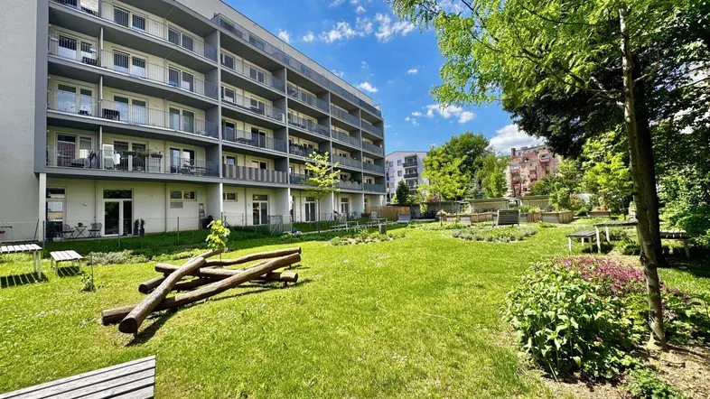 Gepflegter Gemeinschaftsgarten mit Rasenflächen, Sitzgelegenheiten und modernem Wohngebäude im Hintergrund.