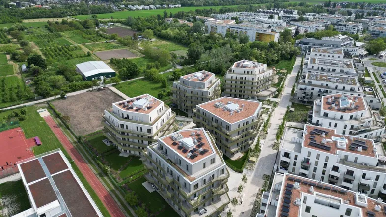 Luftaufnahme eines modernen Wohnkomplexes mit mehreren Gebäuden, Grünflächen und Sportplatz.