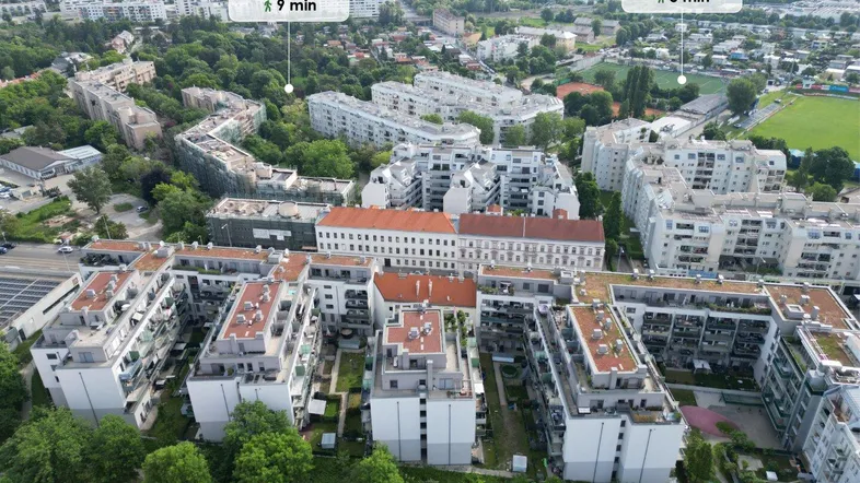 Luftaufnahme einer Wohngegend mit Mehrfamilienhäusern und umliegenden Grünflächen, inklusive Entfernungsangaben zu Parks.