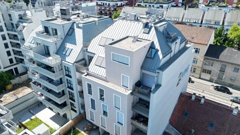 Moderne Wohnanlage mit mehreren Balkonen und Dachterrassen in urbaner Umgebung, umgeben von Grünflächen.
