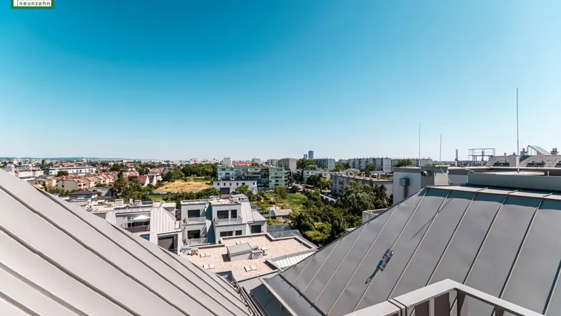 Weitläufiger Blick über die Dächer der Stadt mit grünen Flächen in der Ferne.
