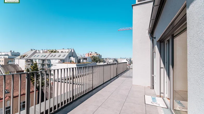 Große Dachterrasse mit Fliesenboden und weitem Blick über die Stadt unter blauem Himmel.