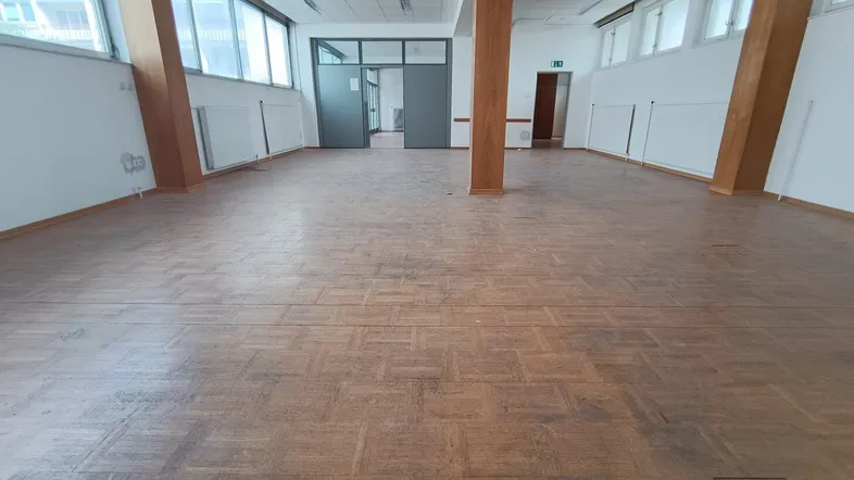 Geräumiger Bürobereich mit Parkettboden, großen Fenstern und Zugang durch Glastüren.