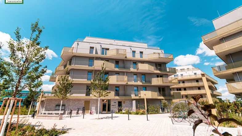 Modernes Mehrfamilienhaus mit vielen Balkonen und gepflegten Außenanlagen unter blauem Himmel.