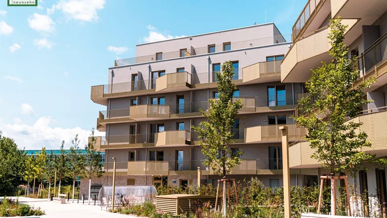 Moderne Wohnanlage mit mehreren Balkonen und gepflegter Grünfläche unter blauem Himmel.