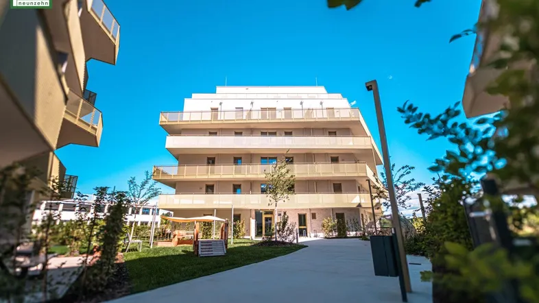 Modernes Mehrfamilienhaus mit Balkonen und gepflegter Außenanlage unter blauem Himmel.