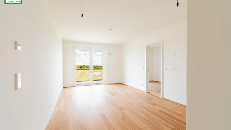 Helles, leeres Zimmer mit Holzboden und Zugang zu einem Balkon mit Weitblick.