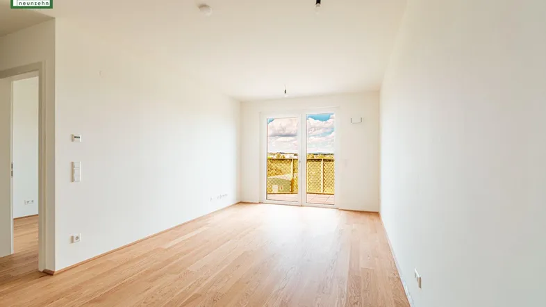 Helles Zimmer mit Holzboden und Zugang zu einem Balkon mit weitem Ausblick.