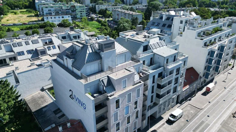 Luftaufnahme eines modernen Wohngebäudes mit mehreren Balkonen und Dachterrassen in städtischer Umgebung.