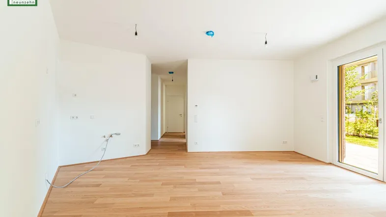 Heller, leerer Raum mit Parkettboden und Zugang zu einem grünen Außenbereich.