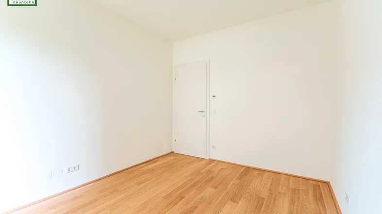 Helles, leeres Zimmer mit hellem Parkettboden und weiß gestrichenen Wänden, bereit zum Einzug.
