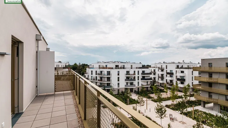 Geräumiger Balkon mit Fliesenboden und Blick auf die moderne Wohnanlage und den begrünten Innenhof.
