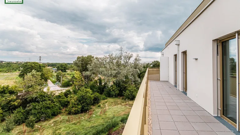 Lange Terrasse mit Fliesenboden und weitem Blick ins Grüne unter bewölktem Himmel.