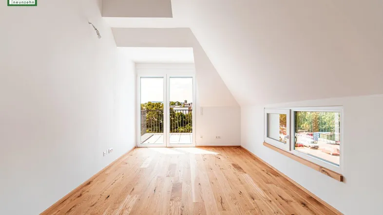Helles Zimmer im Dachgeschoss mit Holzboden, Balkonzugang und schrägen Wänden.