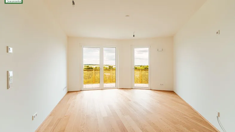 Helles, leeres Zimmer mit Holzboden und Zugang zu einem Balkon mit weitem Blick ins Grüne.
