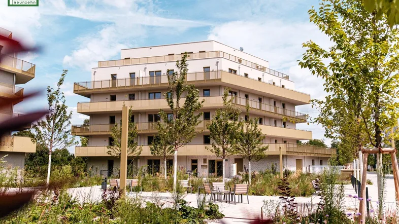 Modernes Wohngebäude mit gestuften Balkonen und gepflegter Grünanlage an einem sonnigen Tag.