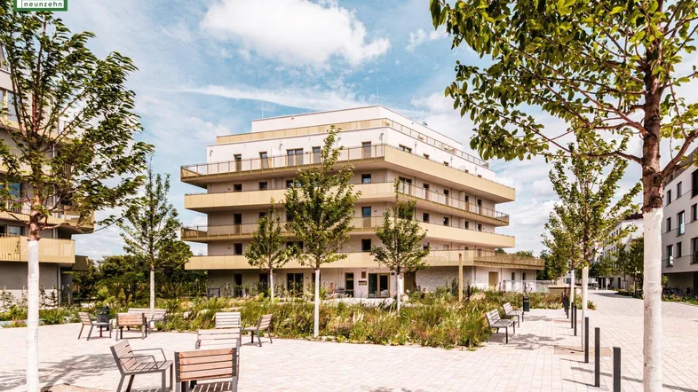Ansicht des modernen Apartmentkomplexes mit gepflastertem Vorplatz und Sitzgelegenheiten im Freien.
