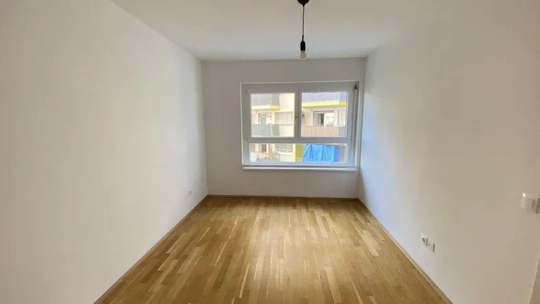 Helles, leeres Zimmer mit Parkettboden und großem Fenster, bereit zur Einrichtung.