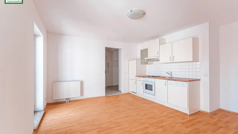 Heller offener Wohnbereich mit integrierter Küchenzeile und Parkettboden, ideal für modernes Wohnen.
