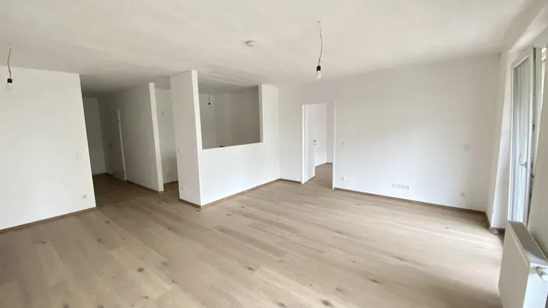 Helles, leeres Zimmer mit hellem Holzboden und weißen Wänden, bereit zur individuellen Gestaltung.