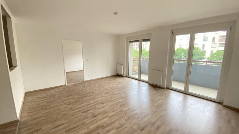Helles, leeres Wohnzimmer mit Laminatboden und Zugang zu einem Balkon.