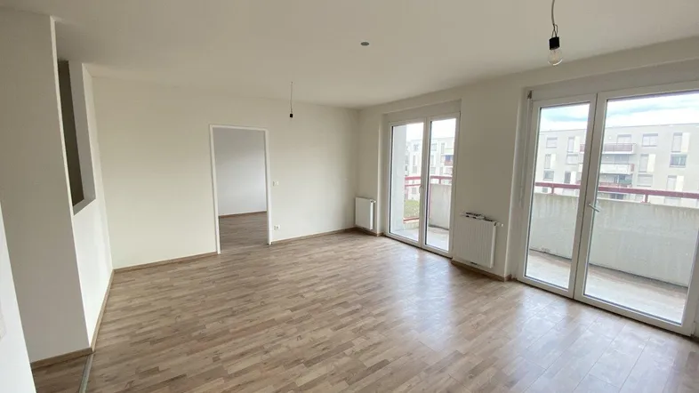Helles Wohnzimmer mit Laminatboden und Zugang zu einem Balkon, bereit zur individuellen Gestaltung.