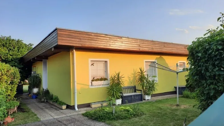 Gelbes Einfamilienhaus mit gepflegtem Vorgarten und Terrasse unter blauem Himmel.